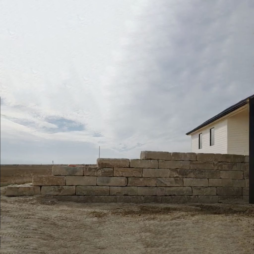 Workers install a large rock retaining wall on a new construction home.