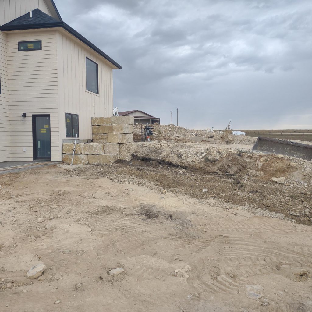 Workers install a large rock retaining wall on a new construction home.